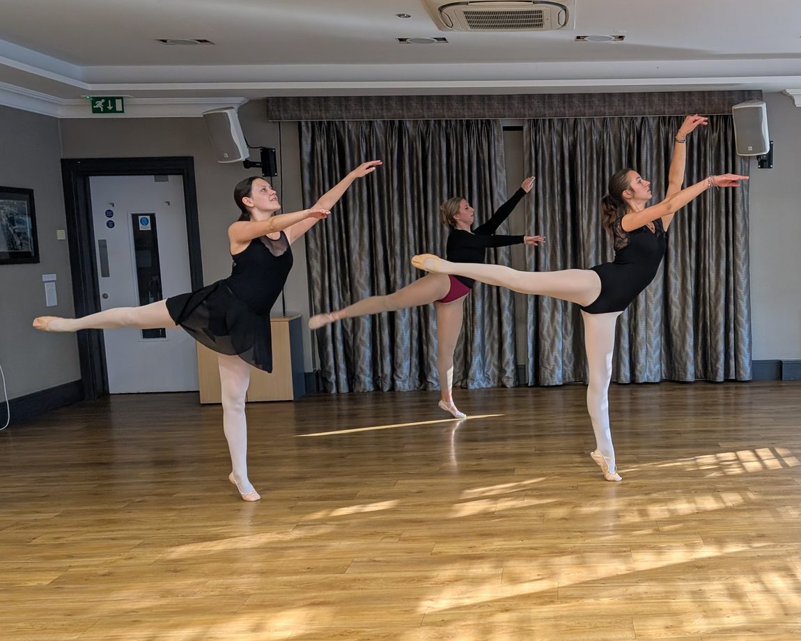 Three senior dancers holding an arabesque in a ballet class